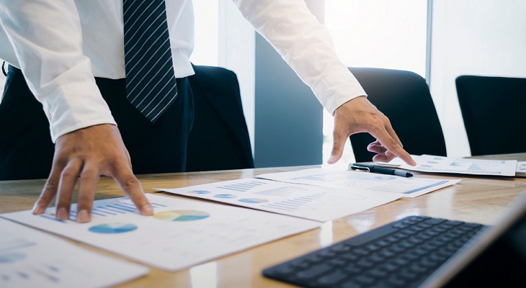A professional examining charts and reports on a desk, indicative of strategic planning or analysis in a business context.
