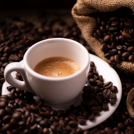 A cup of espresso surrounded by scattered coffee beans with a burlap sack in the background.