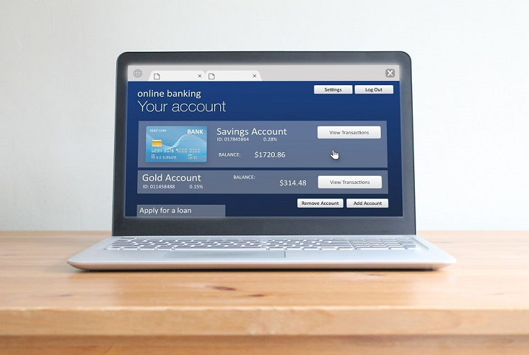 Laptop displaying an online banking interface with accounts and balance information on a wooden desk