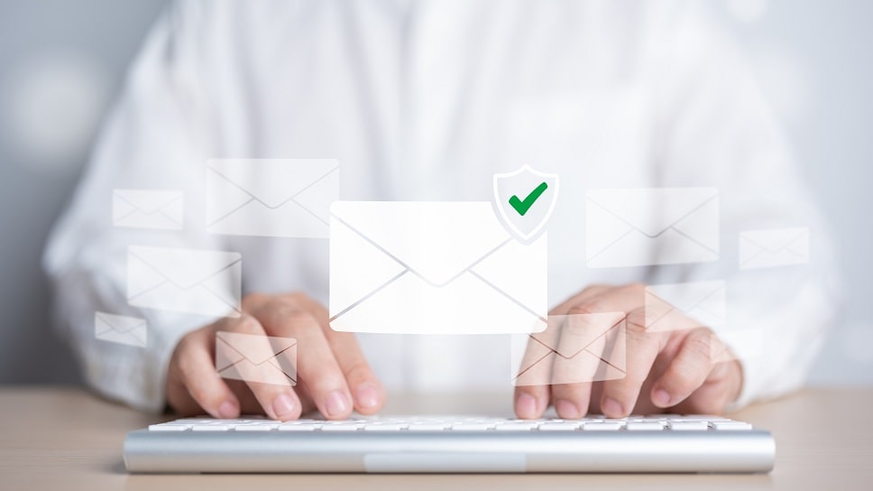 Person typing on a keyboard with floating email icons and a verified check mark, symbolizing secure email communication.