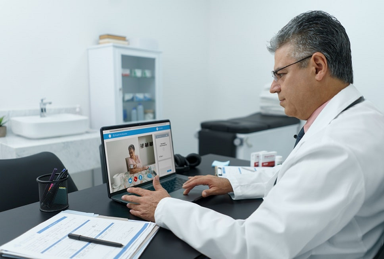 Male doctor conducting a virtual appointment with elderly woman taking her blood pressure 