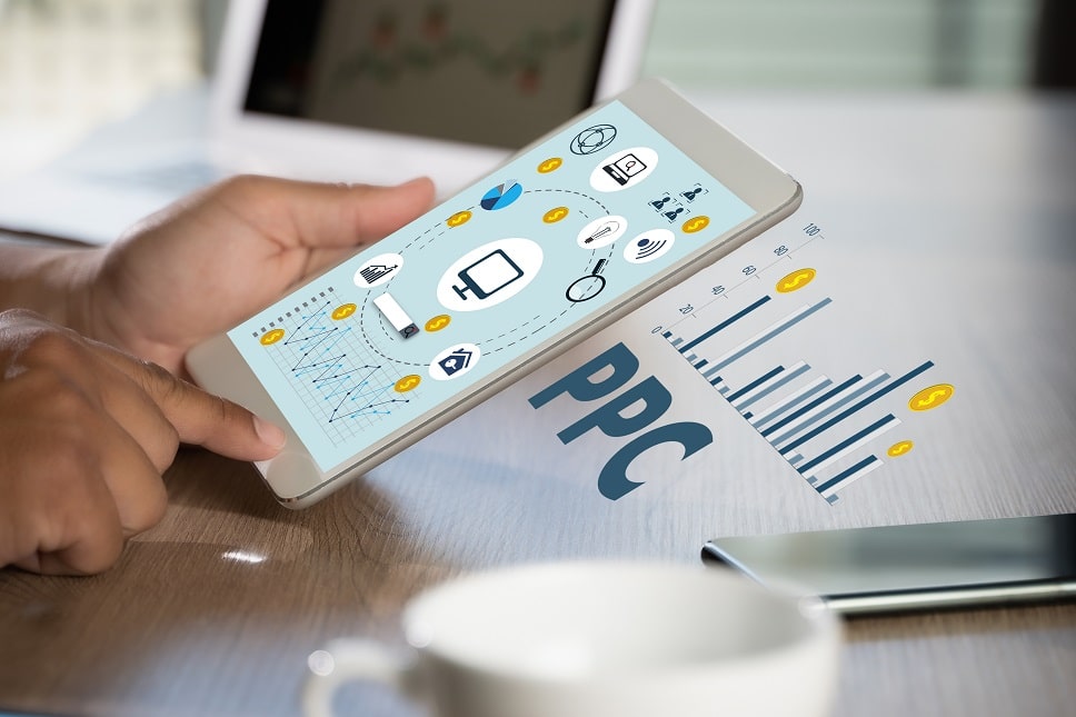 Hands holding a tablet displaying PPC (Pay-Per-Click) marketing analytics and icons, symbolizing digital advertising strategies.
