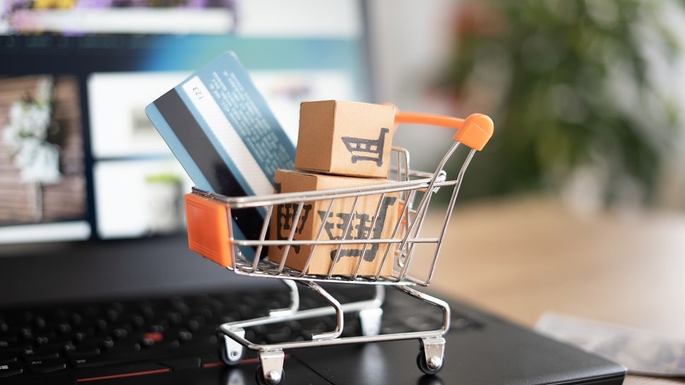 Mini shopping cart filled with boxes and a credit card placed on a laptop, depicting online shopping and ecommerce image
