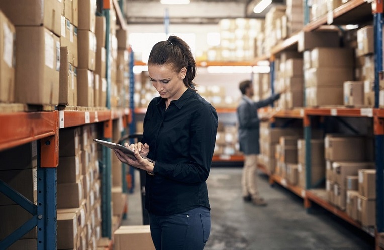 Focused warehouse worker checking inventory with a digital tablet in a busy distribution center aisle.