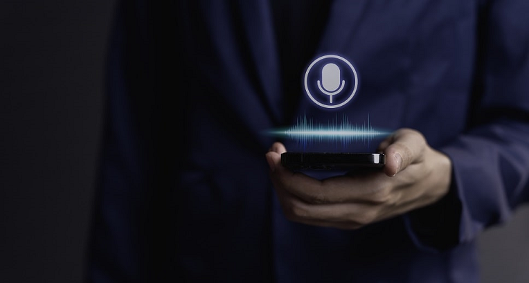 Person in a suit holding a smartphone with a glowing voice control icon, representing voice-activated digital assistance