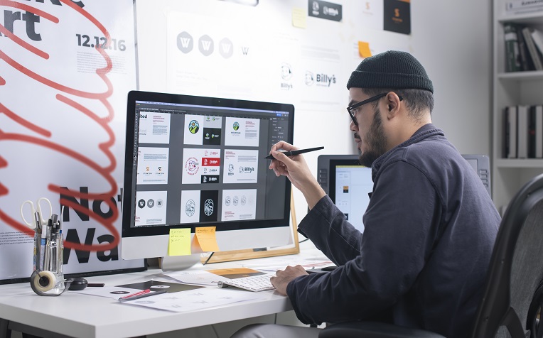 Graphic designer working on a logo project using a stylus and a desktop drawing tablet in a creative workspace.