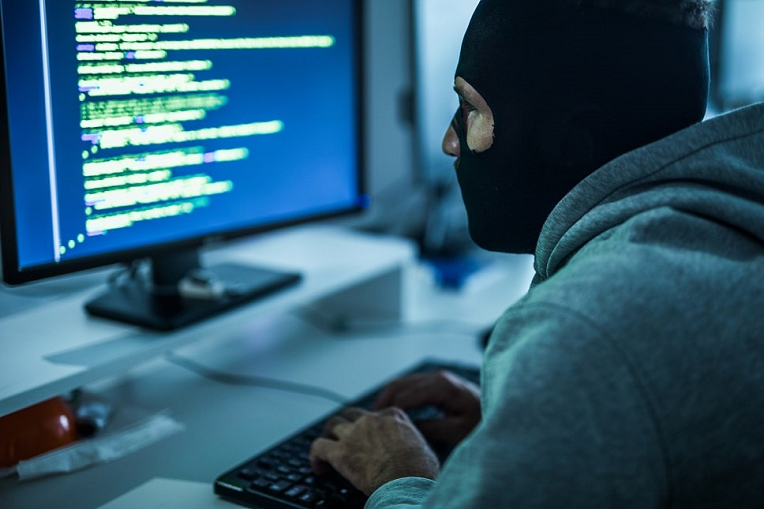 Person with a ski mask using a computer, symbolizing cybersecurity threats.