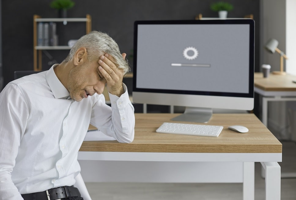 Distressed businessman with hand on forehead facing a computer with a loading screen, indicating website downtime or technical issues.