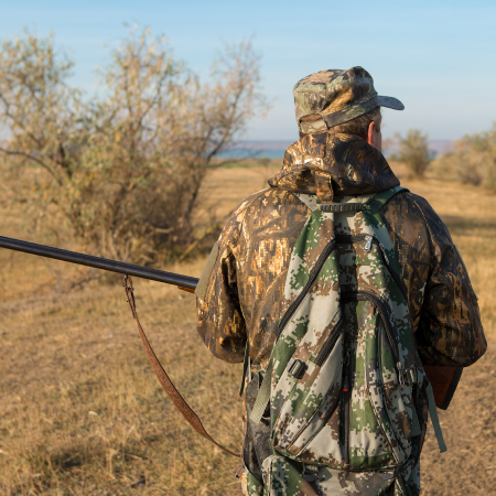 Hunter in camouflage gear with a shotgun over shoulder looking out into the field.